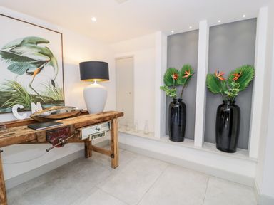 A room with a wooden table holding a lamp and decorations and two black vases with plants placed in wall niches at Capel Mawr Basement 19 in Llanrug