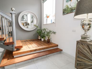 A stair landing area with wooden steps and plants next to a round wall mirror and a cabinet with a silver lamp at Capel Mawr Basement 19 in Llanrug