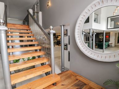 A wooden staircase with metal railings next to a large round mirror in a hallway at Capel Mawr Basement 19 in Llanrug