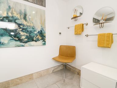 A corner with a brown chair yellow towels on racks two round mirrors and a white cabinet at Capel Mawr Basement 19 Llanrug