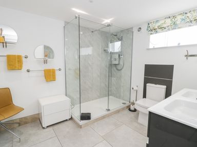 A bathroom with a glass shower enclosure a toilet a double sink a chair and yellow towels at Capel Mawr Basement 19 in Llanrug