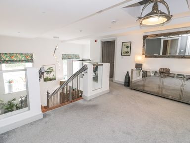 A landing area with a staircase, a mirrored sideboard, a lamp, a large wall mirror, and framed artwork at Capel Mawr, Basement 19 in Llanrug