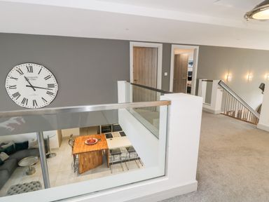 An upstairs hallway with carpet and two wooden doors overlooking a kitchen and living area below at Capel Mawr Basement 19 in Llanrug