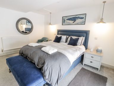 A bedroom with a blue bed, bedside table, armchair, round mirror, whale painting, and two pendant lights at Capel Mawr Basement 19 Llanrug