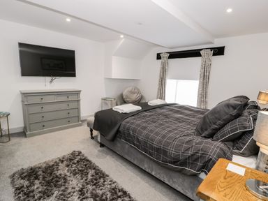 A bedroom with a bed a gray dresser a wall-mounted television and two small side tables at Capel Mawr Basement 19 in Llanrug