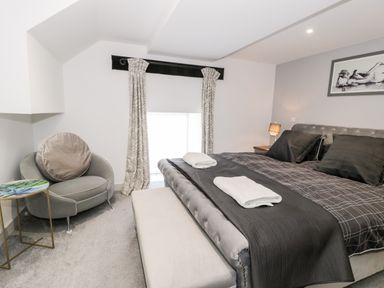 A bedroom with a bed with folded towels an armchair a small side table and curtains at Capel Mawr Basement 19 in Llanrug