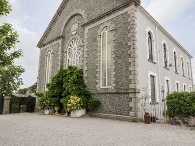 Exterior stone and stucco building with arched windows and greenery at Capel Mawr Basement 19 in Llanrug