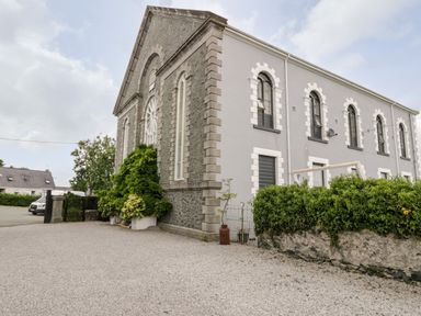 A stone and grey building with arched windows and plants outside at Capel Mawr Basement 19 in Llanrug