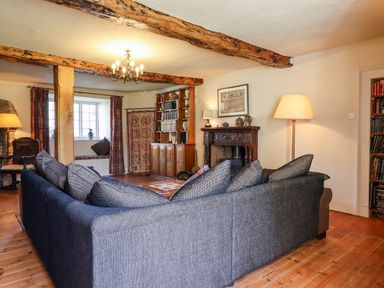 A living room with a large sectional sofa wooden beams a wooden cabinet and a fireplace at Aluric's Hall in Porlock