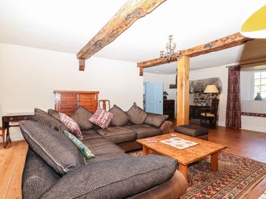 A living room with a brown sectional sofa a wooden coffee table exposed wooden beams and a window at Aluric's Hall in Porlock