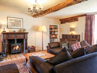 A living room with sofas a wooden coffee table a fireplace wooden beams and a bookshelf at Aluric's Hall in Porlock