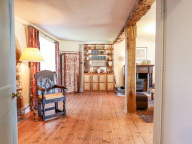 A room with wooden floor a carved wooden chair a floor lamp bookcase with books and ceramics and a fireplace in the background at Aluric's Hall in Porlock