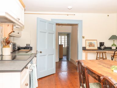 A kitchen with wooden floor a wooden dining table and chairs a blue door and countertop appliances at Aluric's Hall in Porlock