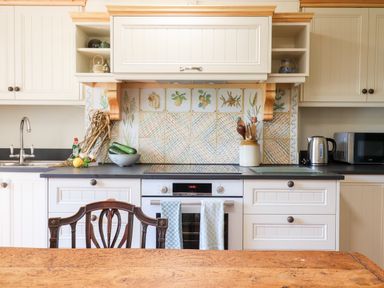 A kitchen with white cabinets black countertop a built in oven and stovetop with decorative tile backsplash and a wooden table with a chair at Aluric's Hall in Porlock