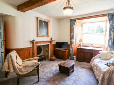 A sitting room with a fireplace TV curtains and furniture at Aluric's Hall in Porlock