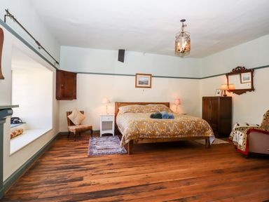 A bedroom with a double bed a chair rugs wooden floor and a window seat at Aluric's Hall in Porlock
