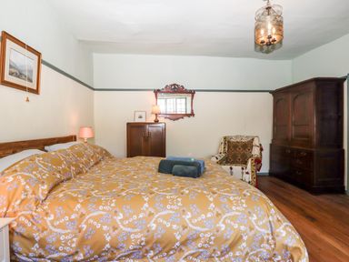 A bedroom with a double bed covered in yellow floral bedding a wooden wardrobe a cabinet an armchair and a wall mirror at Aluric's Hall in Porlock