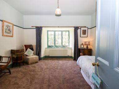 A bedroom with a bed a chair a wooden cabinet a window with curtains and a door with a snoring room sign at Aluric's Hall in Porlock