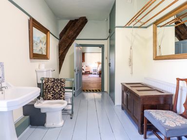A bathroom with a sink bidet toilet wooden chest chair and mirror at Aluric's Hall in Porlock