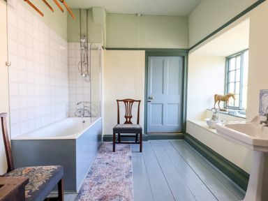 A bathroom with a bathtub a wooden chair a pedestal sink and a window with decorative items at Aluric's Hall in Porlock