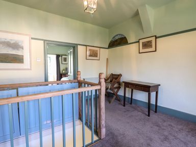 A hallway with blue wooden railing a wooden chair a small wooden desk and framed paintings on the walls at Aluric's Hall in Porlock