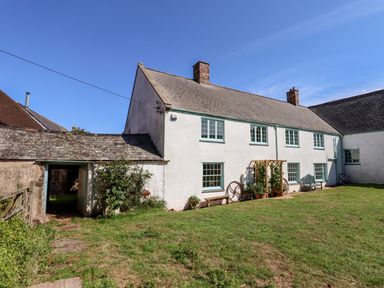 An exterior view of a white two-story house with green-trimmed windows a grassy yard benches and a wooden garden trellis at Aluric's Hall in Porlock