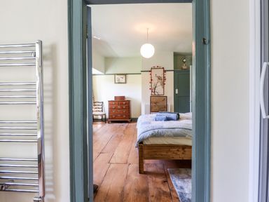 A bedroom with a wooden floor a bed blue bedcovers a wooden dresser two chairs and artwork on the walls at Aluric's Hall in Porlock
