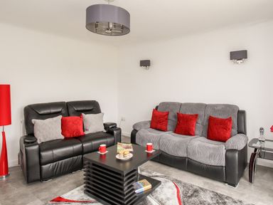 A living room with two sofas a black coffee table with cups and plates and a red floor lamp at Rosamond in Shipton Gorge