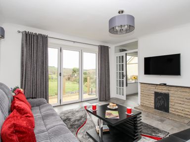 A living room with a gray sofa with red cushions a black coffee table and a wall-mounted TV at Rosamond in Shipton Gorge