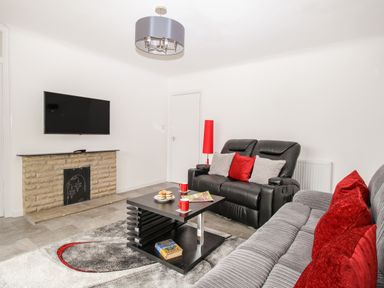 A living room with a wall mounted TV above a stone fireplace two sofas a coffee table and a red lamp at Rosamond in Shipton Gorge
