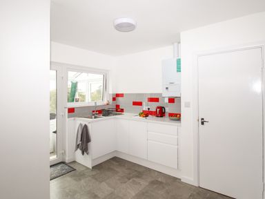 A kitchen with white cabinets a sink a red kettle and tiled backsplash at Rosamond in Shipton Gorge
