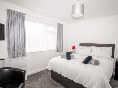 A bedroom with a double bed with towels on it a black chair a chest of drawers and grey curtains at Rosamond in Shipton Gorge