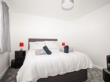 A bedroom with a double bed with white bedding two bedside tables with red lamps and grey curtains at Rosamond in Shipton Gorge