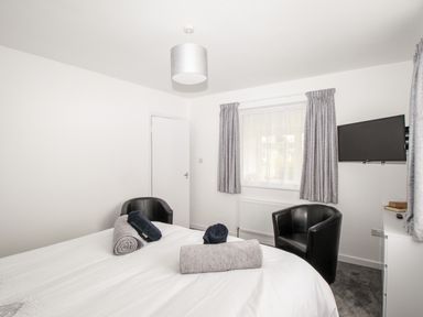 A bedroom with a bed two black chairs a window with curtains and a wall-mounted TV at Rosamond in Shipton Gorge