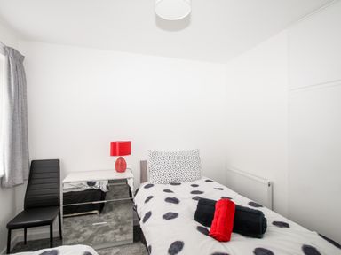 A bedroom with a single bed a chest of drawers with a red lamp a black chair and towels on the bed at Rosamond in Shipton Gorge