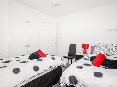 A bedroom with two single beds with black and white polka dot bedding a black chair and bedside table with a red lamp at Rosamond in Shipton Gorge
