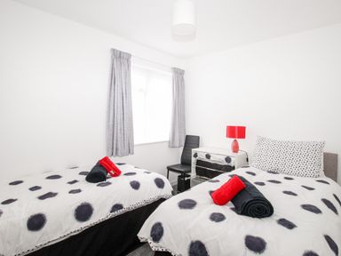 A bedroom with two single beds a black chair a white drawer and a red lamp at Rosamond in Shipton Gorge