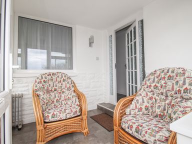 A small room with wicker chairs with patterned cushions and a glass door at Rosamond in Shipton Gorge