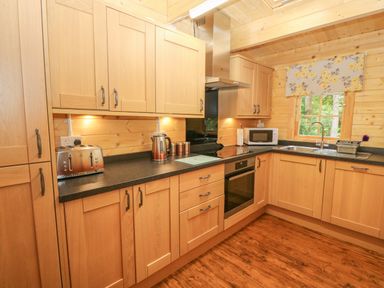A kitchen with wooden cabinets a toaster kettle microwave oven stove and a window at Bryn Derwen Lodge in Bethesda