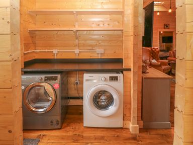 A laundry area with a washing machine and dryer under a black countertop in a wooden cabin at Bryn Derwen Lodge in Bethesda