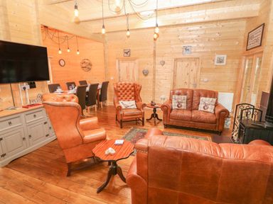 A lounge area with leather armchairs and sofas a wooden coffee table a dining table with chairs and a wall mounted TV at Bryn Derwen Lodge in Bethesda