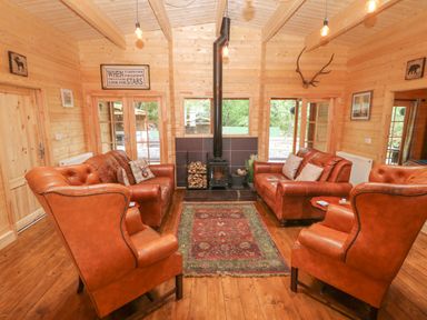 A living room with leather sofas armchairs a wood stove and a rug at Bryn Derwen Lodge in Bethesda