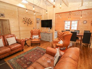 A living room with leather sofas and armchairs a wooden floor a wall-mounted television and a dining table with chairs at Bryn Derwen Lodge in Bethesda