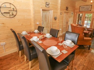 A dining area with a wooden table set for six and leather chairs in a wooden cabin with a living room in the background at Bryn Derwen Lodge in Bethesda