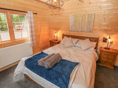 A bedroom with a double bed two bedside tables with lamps a window and wooden walls at Bryn Derwen Lodge in Bethesda