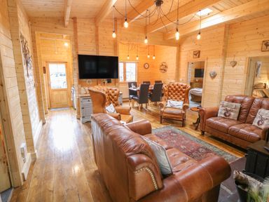 A living room with leather sofas and armchairs a rug a dining table with chairs and a wall-mounted TV at Bryn Derwen Lodge in Bethesda
