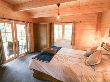 A bedroom with a bed pillows wooden wardrobe carpet and patio doors at Bryn Derwen Lodge in Bethesda