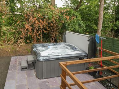 An outdoor hot tub with bubbling water on a tiled patio surrounded by trees and a green fence at Bryn Derwen Lodge in Bethesda