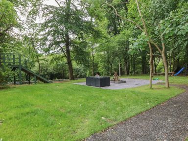 A grassy garden area with trees a slide a swing and a fire pit with seating at Bryn Derwen Lodge in Bethesda