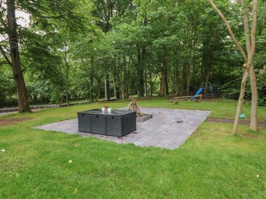 An outdoor patio area with a black wicker table and chairs on gray tiles surrounded by grass and trees at Bryn Derwen Lodge in Bethesda